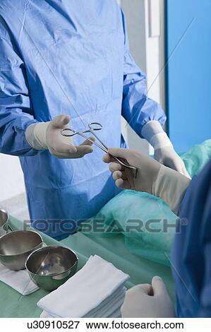 Stock Photo - Nurse handing forceps to surgeon in operating room. Fotosearch
