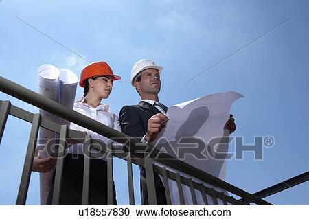 Professionals holding plans at construction site View Large Photo Image Stock Image - Professionals holding plans at construction site. Fotosearch