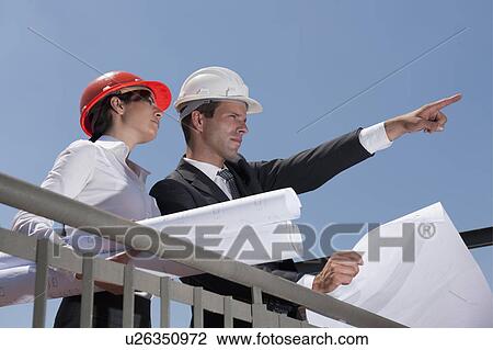 Professionals holding plans at construction site View Large Photo Image Stock Image - Professionals holding plans at construction site. Fotosearch
