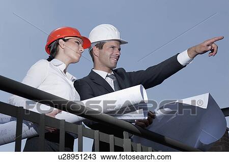 Professionals holding plans at construction site View Large Photo Image Stock Image - Professionals holding plans at construction site. Fotosearch