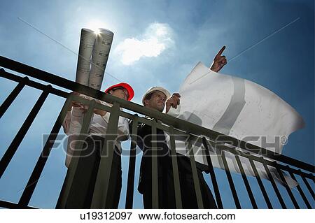 Stock Photo - Professionals holding plans at construction site. Fotosearch