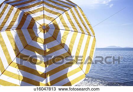 Stock Image - Silhouette of couple on the beach behind umbrella. Fotosearch