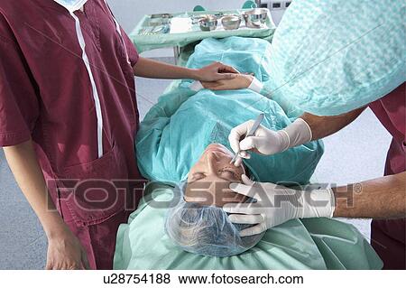 Stock Photo - Surgeon with scalpel on patient's face.. Fotosearch