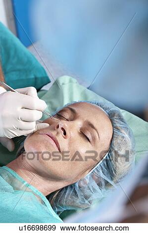 Stock Photo - Surgeon's hand with scalpel to patient's face. Fotosearch