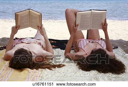 Stock Image - Two female young adults reading books on beach. Fotosearch