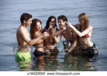 Stock Photo - Two male and three female young adults toasting in sea. Fotosearch