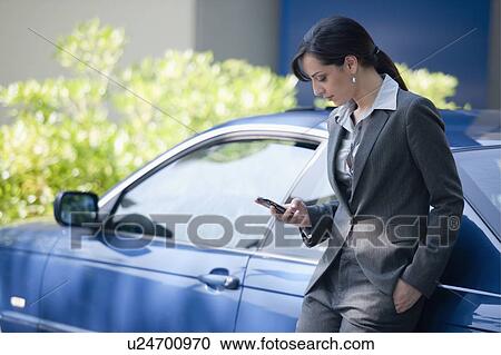 Woman in suit next to car looking at smartphone View Large Photo Image Stock Image - Woman in suit next to car looking at smartphone. Fotosearch