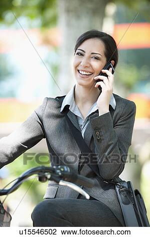 Stock Image - Woman in suit on bicycle talking on cellphone. Fotosearch