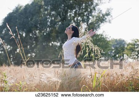 Stock Image - Woman with arms stretched out in wheat field. Fotosearch