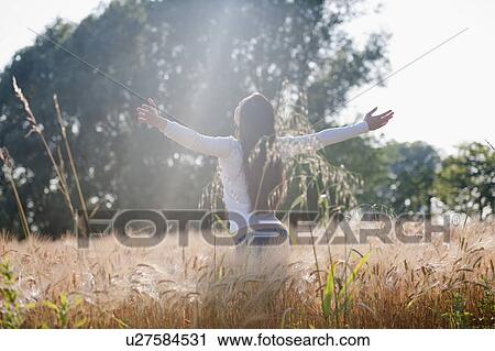 Stock Image - Woman with arms stretched out in wheat field. Fotosearch
