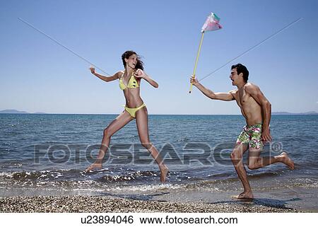 Stock Photograph - Young adult male chasing female on beach. Fotosearch