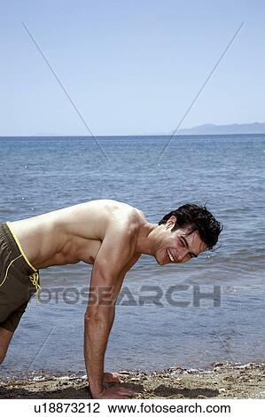 Stock Image - Young adult male doing pushups on beach. Fotosearch