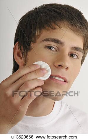 Stock Photograph - Young male adult cleaning face with cotton pad. Fotosearch