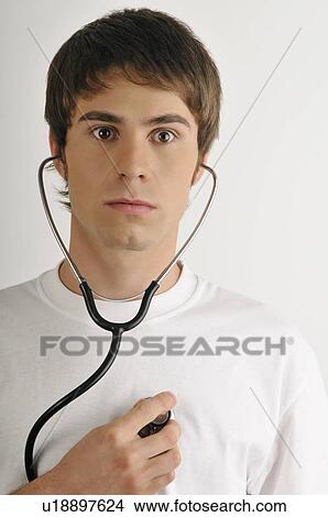 Picture - Young male adult; listening to his heart with stethoscope. Fotosearch
