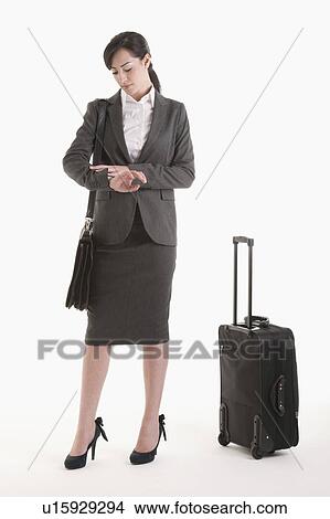 Young woman in suit with wheeled suitcase looking at watch View Large Photo Image Picture - Young woman in suit with wheeled suitcase looking at watch. Fotosearch