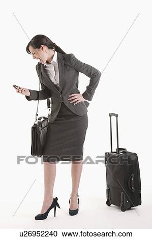 Stock Image - Young woman in suit with wheeled suitcase screaming at phone. Fotosearch