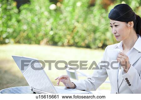 Stock Image - Businesswoman drinking coffee and using laptop. Fotosearch