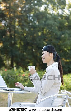Stock Photo - Businesswoman drinking coffee and using laptop. Fotosearch