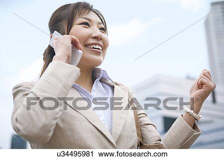 Stock Image - Businesswoman on cell phone making a fist, low angle view. Fotosearch