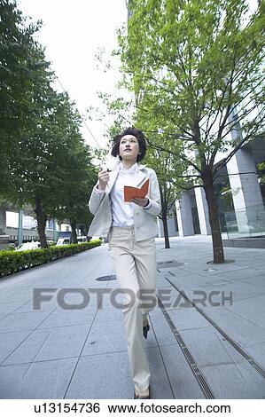 Stock Photograph - Businesswoman running and holding a diary. Fotosearch