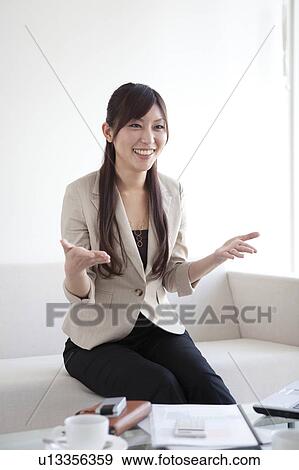 Stock Photo - Businesswoman sitting on sofa talking. Fotosearch