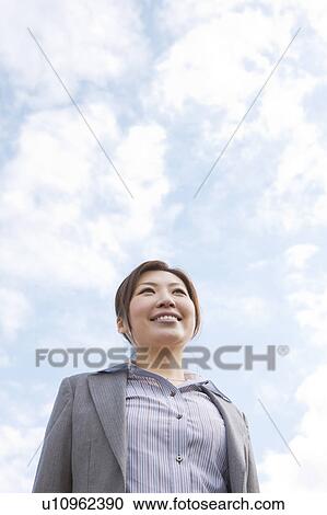 Stock Image - Businesswoman standing and smiling, low angle view. Fotosearch