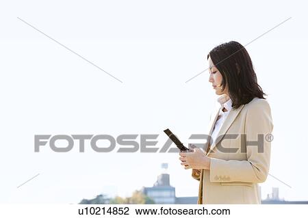 Stock Image - Businesswoman using a cell phone on rooftop. Fotosearch