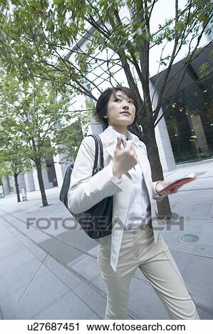 Stock Image - Businesswoman walking and holding a diary. Fotosearch