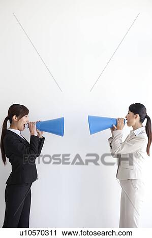 Stock Image - Businesswomen holding megaphone and screaming at each other. Fotosearch