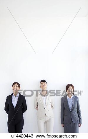 Stock Image - Businesswomen standing side by side looking up. Fotosearch