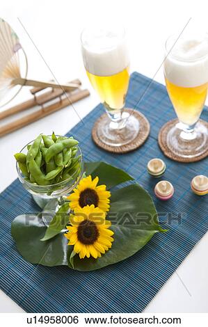 Stock Photograph - Glasses of beer, edamame, sunflowers, tops and fan on place mat. Fotosearch