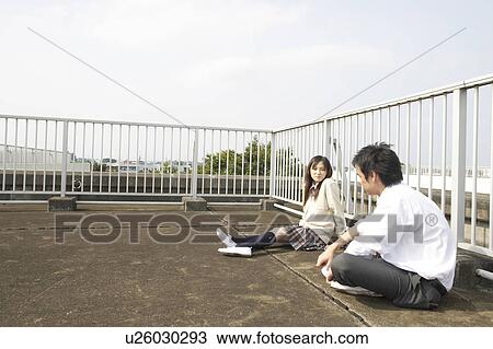 Stock Image - High school students talking on rooftop, Japan. Fotosearch