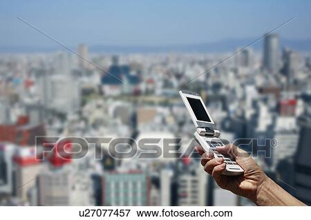 Man's hand holding a cell phone and cityscape of Osaka, Osaka Prefecture, Honshu, Japan View Large Photo Image Stock Photo - Man's hand holding a cell phone and cityscape of Osaka, Osaka Prefecture, Honshu, Japan. Fotosearch