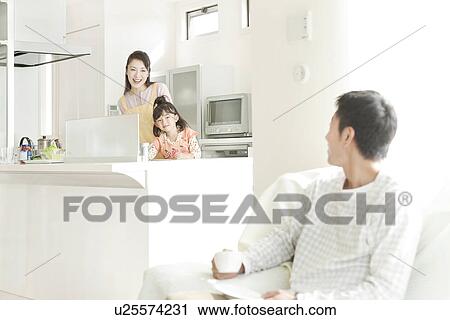 Stock Image - Mother and Daughter Cooking Kitchen and Talking to Father. Fotosearch