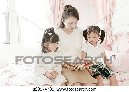 Stock Photography - Mother Reading Book to Her Two Daughters. Fotosearch