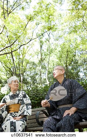 Stock Image - Senior couple wearing Yukata sitting on bench. Fotosearch
