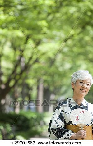 Senior woman holding a fan wearing Yukata View Large Photo Image Stock Photo - Senior woman holding a fan wearing Yukata. Fotosearch