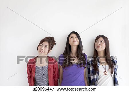 Stock Photo - Three women standing side by side and looking up. Fotosearch