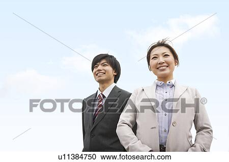 Stock Image - Two Businesspeople Standing Below Blue Sky. Fotosearch