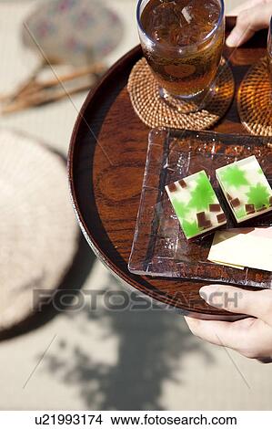 Picture - Woman holding a tray with glass of barley tea and sweet food. Fotosearch