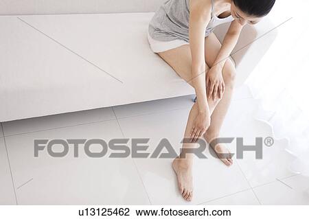 Stock Image - Woman sitting on sofa massaging leg. Fotosearch