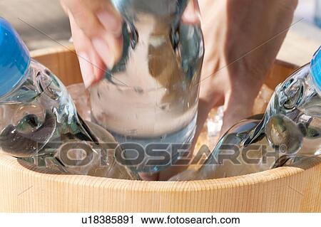 Stock Image - Woman taking out a bottle of soda from a bucket. Fotosearch