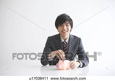 Young businessman putting coin into piggy bank View Large Photo Image Stock Image - Young businessman putting coin into piggy bank. Fotosearch