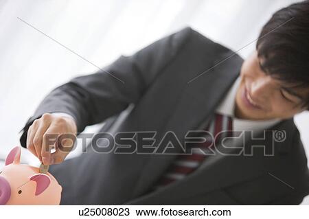 Young businessman putting coin into piggy bank View Large Photo Image Stock Image - Young businessman putting coin into piggy bank. Fotosearch