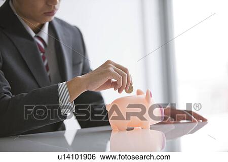 Young businessman putting coin into piggy bank View Large Photo Image Stock Photograph - Young businessman putting coin into piggy bank. Fotosearch
