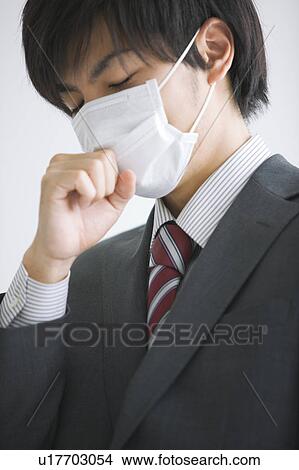 Picture - Young businessman wearing flu mask coughing. Fotosearch