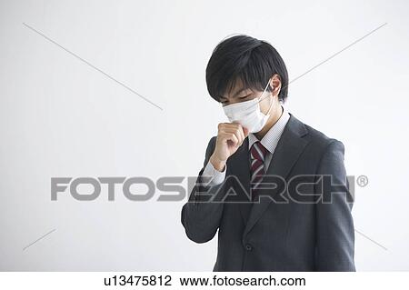 Stock Image - Young businessman wearing flu mask coughing. Fotosearch