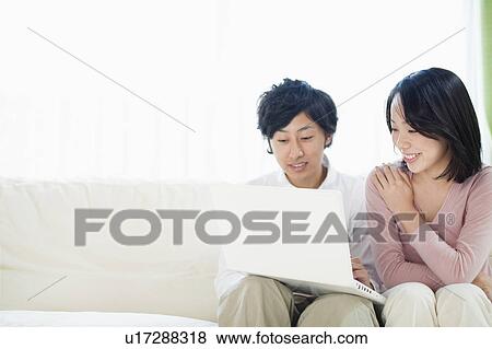 Stock Photo - Young Couple Using Laptop on Sofa. Fotosearch