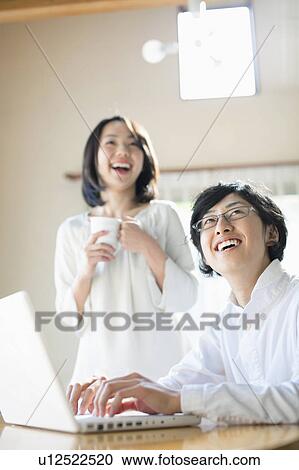Stock Image - Young Man Using Laptop, Girlfriend in Background. Fotosearch