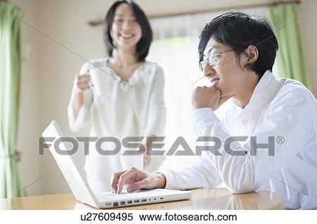 Stock Photography - Young Man Using Laptop, Girlfriend in Background. Fotosearch